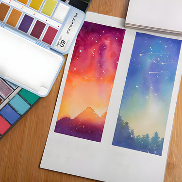 Set di colori ad acquerello Fuumuui da 60 colori aperto, che mostra vivaci cialde di vernice accanto a due dipinti ad acquerello finiti di cieli e paesaggi colorati, evidenziando i ricchi pigmenti.