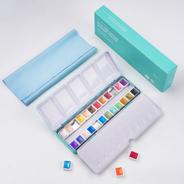 Fuumuui 24-Color Glitter Solid Watercolor Paint Set with vibrant pans in an open turquoise metal tin, including a cleaning cloth and product packaging.