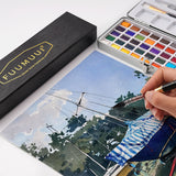 Hand, die eine Aquarellszene mit dem Fuumuui x Svetlin Sofroniev Limited Edition Dual-Tip Travel Brush malt, zusammen mit einer Fuumuui Art Supplies Aquarellpalette und einer Master Series Pinselbox.