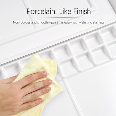 Une main nettoie la palette d'aquarelle professionnelle Fuumuui à 47 godets, mettant en évidence sa surface en plastique antiadhésive, semblable à de la porcelaine, non poreuse et lisse pour un levage facile de la peinture et aucune coloration.