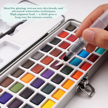 Set di acquerelli portatile a 50 colori Fuumuui con una mano che attiva una vivace cialda rossa utilizzando un pennello ad acqua, che mostra i colori solidi ad alta pigmentazione nella sua custodia da viaggio in metallo.