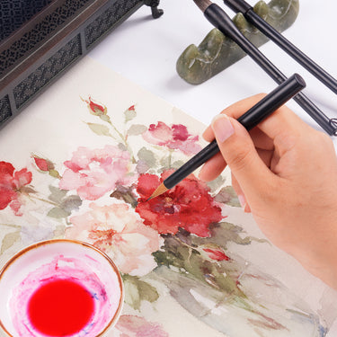 Die Hand eines Künstlers malt rote Aquarellrosen mit einem Fuumuui Portable Split-Body Weasel Hair Brush, einem idealen Fuumuui Art Supplies Reise-Kalligraphiepinsel für detaillierte Kunstwerke.