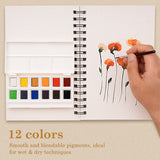 Fuumuui Tragbares 12-Farben-Aquarellfarben-Set mit Palette und Pinsel, in Verwendung gezeigt, wie eine Hand leuchtend orangefarbene Blumen auf ein Skizzenbuch malt, wobei die glatten, mischbaren Fuumuui-Kunstmaterialien hervorgehoben werden.