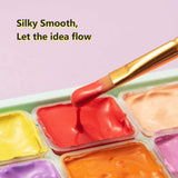 Fuumuui Set di colori Gouache con un pennello che si immerge in una vernice rossa liscia come la seta, evidenziando i 24 colori vivaci nella tavolozza.