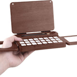 Fuumuui Travel Watercolor Palette, a foldable wooden 24-grid art supply, held in hand, open to reveal a mixing area and space for 2 sable travel watercolor brushes.