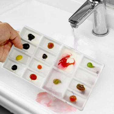 Palette de peinture en céramique pour artiste Fuumuui avec plusieurs godets contenant des peintures vibrantes, nettoyée sans effort sous l'eau courante.