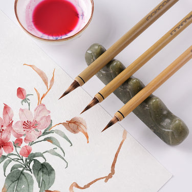 Fuumuui 3-teiliges Aquarellpinsel-Set mit einer Mischung aus natürlichem Wiesel- und Kaninchenhaar, kurzen Spitzen für Präzision und Kontrolle, ausgestellt neben einem floralen Aquarellgemälde und Künstlerbedarf.