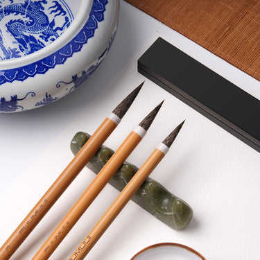 Fuumuui professionelle Kalligraphiepinsel, handgefertigt mit hochwertigem Tierhaar, ruhen auf einer Jade-Pinselablage neben einem blauen und weißen Drachen-Tintenstein.