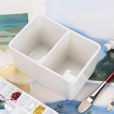 Fuumuui weißes Zweikammer-Keramik-Pinselwaschbecken, perfekt für Aquarell- und Acrylmalerei, gezeigt mit einem Pinsel und einer Palette.