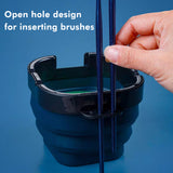 Fuumuui Multifunktionaler, faltbarer Pinselwascheimer, der sein offenes Lochdesign veranschaulicht, wobei eine Hand Pinsel zur sicheren Aufbewahrung einsetzt.