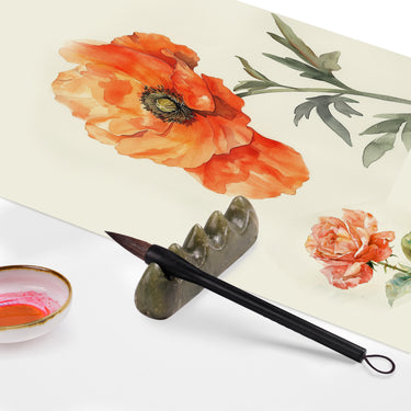 Pinceau Fuumuui en poils d'écureuil gris avec pointe souple, manche lisse et cordon de suspension, reposant sur un porte-pinceau en pierre à côté de peintures de fleurs à l'aquarelle vibrantes et d'un plat de peinture orange.