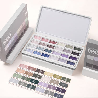Ensemble de peinture aquarelle semi-opaque 24 couleurs Fuumuui avec des couleurs atténuées, ouvert dans une boîte en métal blanc, montrant les godets de peinture individuels et une feuille d'étiquettes d'échantillons de couleurs détaillée. Fournitures d'art Fuumuui.