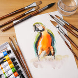 9 pennelli da acquerello professionali Fuumuui, inclusi Needle Tip e Mop, esposti con un vivace dipinto di un pappagallo e colori ad acquerello.