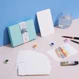 FUUMUUI Aquarellpostkarten mit Umschlag, 100% Baumwolle & kaltgepresst, mit einer bemalten Postkarte neben leeren Karten, Aquarellfarben, Pinseln und anderem FUUMUUI-Kunstbedarf, bereit für die Gestaltung.