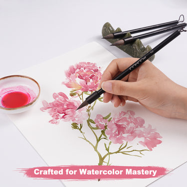 Die Hand eines Künstlers, der mit einem Fuumuui Eichhörnchenhaar-Kalligraphiepinsel rosa Aquarellblumen malt. Ein Set aus 4 Fuumuui handpolierten Rosenholzpinseln mit einem robusten, flachen Aufhängedesign ist im Hintergrund ausgestellt und repräsentiert Fuumuui Art Supplies, die für die Aquarellmalerei entwickelt wurden.