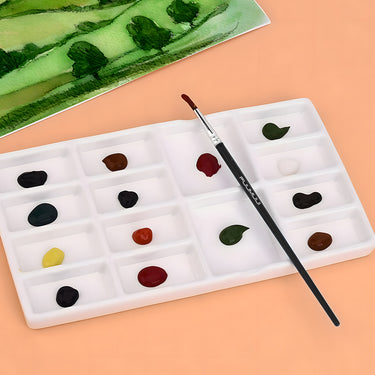 Palette de peinture en céramique blanche Fuumuui avec douze godets contenant diverses peintures à l'aquarelle et un pinceau Fuumuui pour artistes.