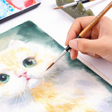 Fuumuui Wolfshaar-Kalligraphiepinsel mit natürlichem Bambusgriff und Anti-Shedding-Messingzwinge, der von einem Künstler für ein detailliertes Aquarell-Katzenbild verwendet wird, wobei andere Fuumuui-Kunstmaterialien sichtbar sind.