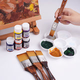Fuumuui Vielseitiges Flachpinselset 4-teilig (20/30/40/50mm) mit hochwertigen synthetischen Borsten und Holzgriffen, gezeigt mit einer Hand, die mit einem Pinsel lebendige Farben in einer Farbpalette mischt. Mehrere Fuumuui Kunstbedarf, darunter Farbflaschen und eine Staffelei, vervollständigen die kreative Malszene.