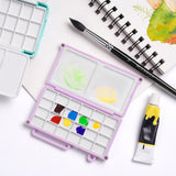 Palette de mélange d'aquarelle mini Fuumuui violette avec 24 godets et plateaux de mélange doubles, montrée ouverte avec des peintures à l'aquarelle, un pinceau Fuumuui et un carnet de croquis, parfaite pour l'art portable et les fournitures de peinture.