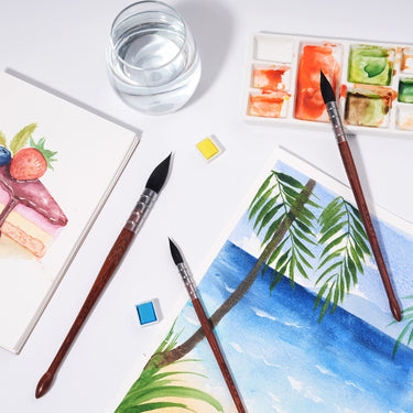 Pennelli a punta tonda in pelo di scoiattolo naturale FUUMUUI per pittura ad acquerello, esposti accanto a una tavolozza, acqua e opere d'arte finite vivaci che raffigurano un dessert colorato e una serena scena di spiaggia. Forniture artistiche Fuumuui essenziali.