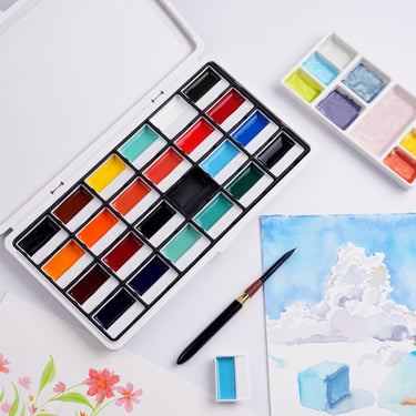 Fuumuui 24-Color Opaque Semi-Solid Watercolor Paint Set - Earthy Color, open for use as Fuumuui Art Supplies, with a watercolor brush, mixing palette, and completed paintings of clouds and flowers.