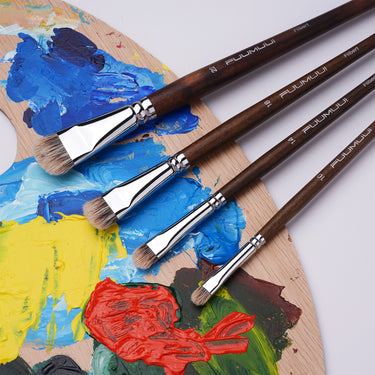 Set di pennelli Filbert FUUMUUI da 4 pezzi con setole di tasso e manici in legno marrone su una tavolozza d'artista con vivaci colori a olio e acrilici.