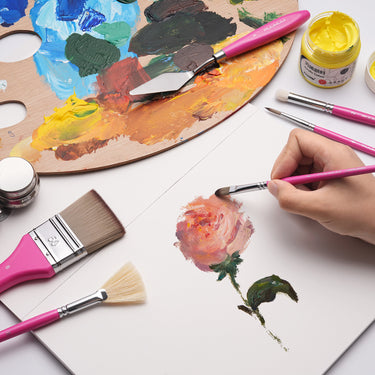Ensemble de pinceaux de mélange acrylique professionnels Fuumuui & Samantha Anderson avec des manches roses en cours d'utilisation, peignant une rose à côté d'une palette d'artiste avec des peintures acryliques vibrantes et un couteau à palette Fuumuui.