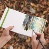 Artista che dipinge un paesaggio forestale con un pennello Fuumuui nel blocco per acquerello Fuumuui - 5.5x5.5" Verde Erba, 100% cotone, pressato a freddo - dimostrando i materiali artistici Fuumuui di alta qualit¨¤.