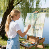 Artiste blonde peignant un paysage à l'aquarelle avec les fournitures d'art Fuumuui, utilisant un pinceau à pointe longue en poils d'animaux de l'ensemble Fuumuui 4 pièces avec un manche en bambou, adapté à l'aquarelle et à la calligraphie.