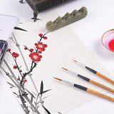 Fuumuui Wolfshaar-Kalligraphiepinsel, ein 3er-Set mit natürlichen Bambusgriffen und Messingzwingen, werden auf Papier neben einer eleganten Malerei im Sumi-e-Stil von roten Pflaumenblüten und Bambus ausgestellt, zusammen mit traditionellen Fuumuui-Kunstmaterialien wie einer Jade-Pinselablage und einem Tintenfass.