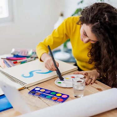 Fuumuui 5pcs Squirrel Hair Hake Flat Watercolor Brushes in use by an artist painting with a palette and sketchbook.