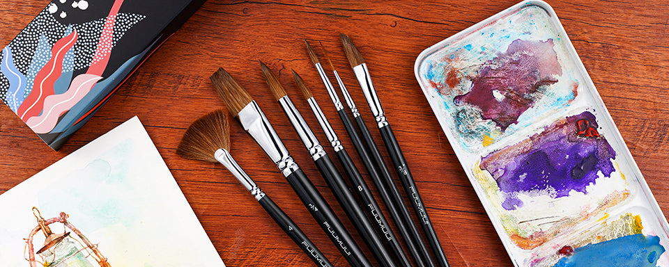 Fuumuui 7pcs professional Kolinsky sable watercolor brush set with fan, flat, and round detail brushes. Arranged on wood with a travel watercolor palette and artwork, perfect for professional artists.