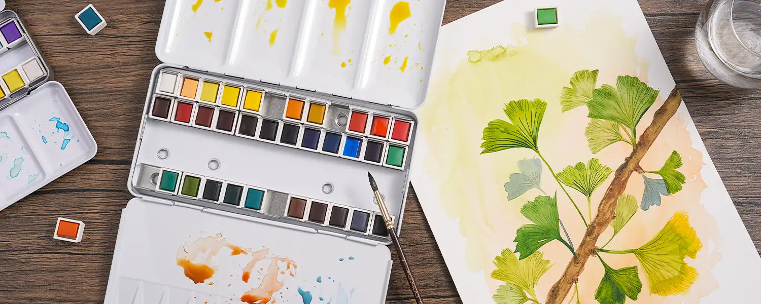 The FUUMUUI 36-color half-pan solid watercolor paint set next to a ginkgo leaf watercolor artwork.