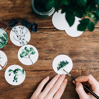 Fuumuui professional nylon detail brush creating intricate watercolor tree paintings, surrounded by finished tree art on a wooden desk.