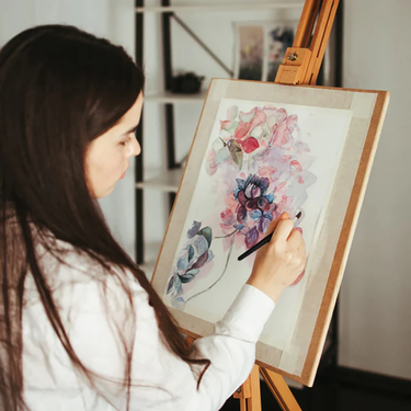 Frau verwendet Fuumuui professionelle Aquarellpinsel, um ein lebendiges Blumenkunstwerk auf einer Staffelei zu malen.