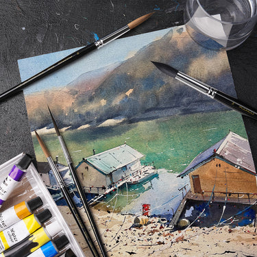Fuumuui & Svetlin Sofroniev Master’s Set Ultimate Collection mit professionellen Aquarellpinseln und Farbtuben, die um ein lebhaftes Landschaftsgemälde von Häusern an einem See und Bergen angeordnet sind.