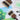 Two Fuumuui wide flat brushes on a watercolor painting of a tree, alongside a watercolor tube and palette.