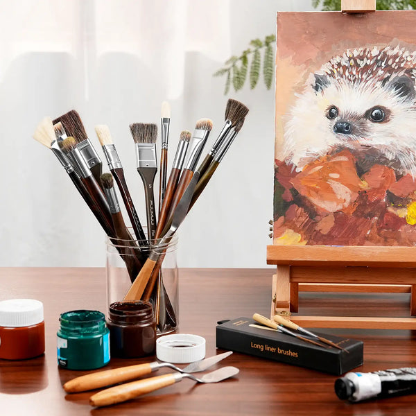 Professional Oil Paint Brush set with natural bristle and synthetic nylon brushes in a jar. Includes palette knives and long liner brushes on a desk with oil paint jars and a hedgehog painting on an easel.