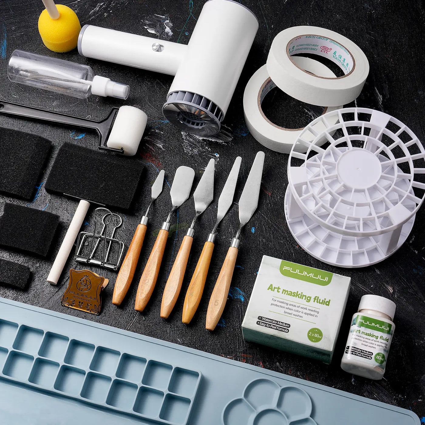 Essential art supplies including Fuumuui Art masking fluid, stainless steel palette knives, masking tape, foam brushes, a spray bottle, and a paint brush cleaner rack for professional watercolor and acrylic artists.