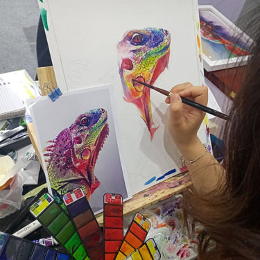 Artist painting a vibrant rainbow iguana using a Fuumuui Travel Portable Watercolor Set Assorted Colors Pocket Kit, displaying the rich pigments and multiple palettes.